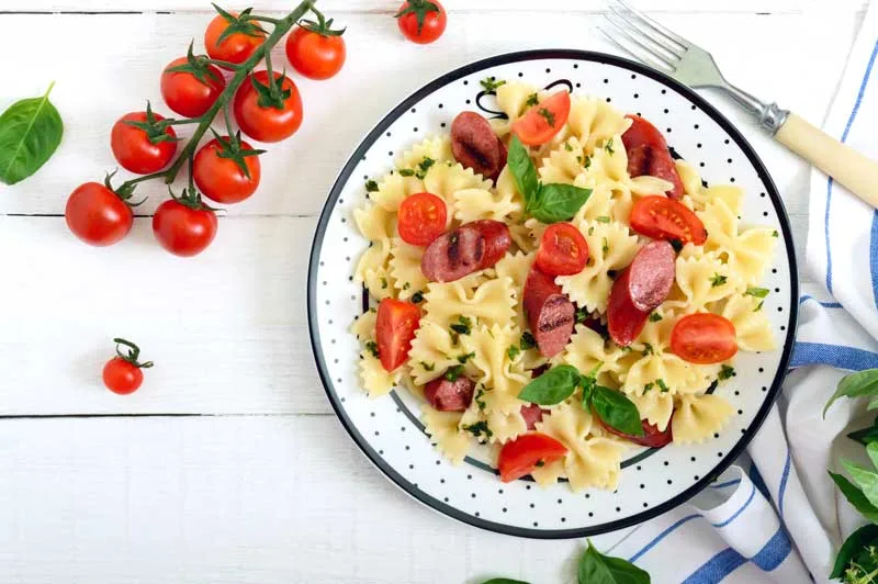 Pastasalade farfalle met stukken gegrilde worstjes, verse cherry tomaten en basilicum